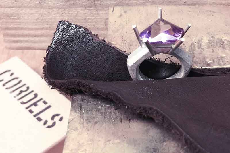 Silberring mit violettem Edelstein auf schwarzem Lederpolster, in der Ecke ein „CORDELS“-Etikett.