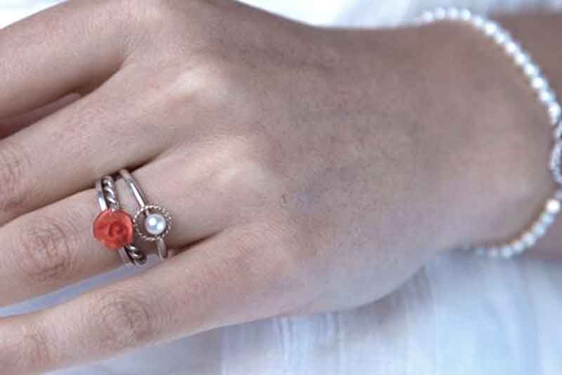 Hand mit silbernen Ringen und einem Perlenarmband. Ein Ring hat einen roten Stein, ein anderer eine Perle.