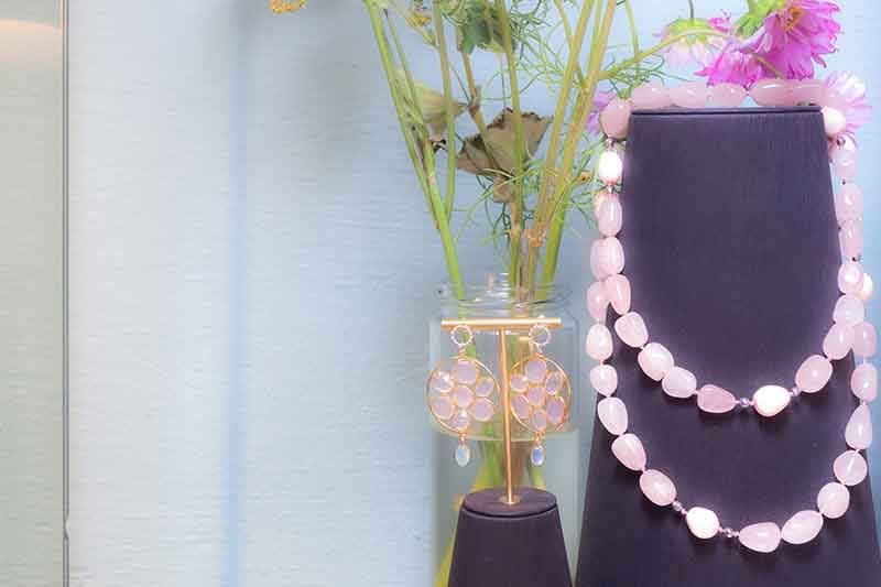 Rosenquarzschmuck in einer Vase mit getrockneten Blumen. Hellrosa Halskette und Ohrringe auf einem Ständer.