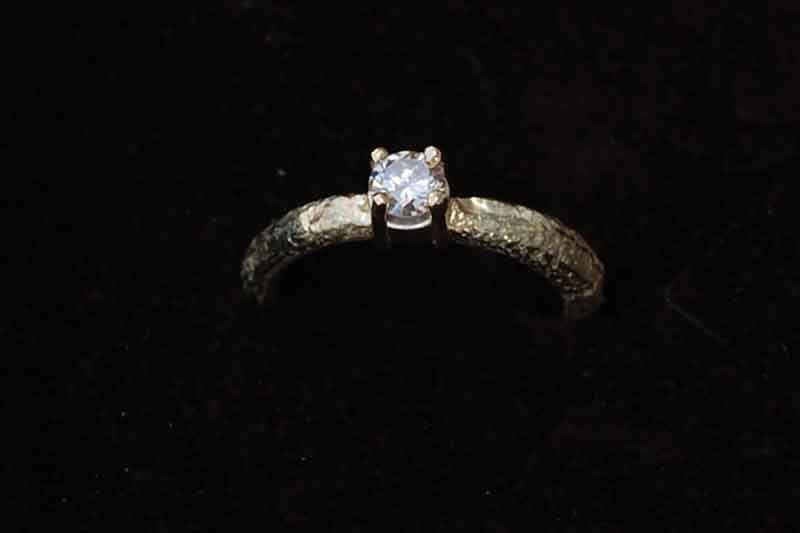 Goldring mit einem kleinen Diamanten auf schwarzem Hintergrund.