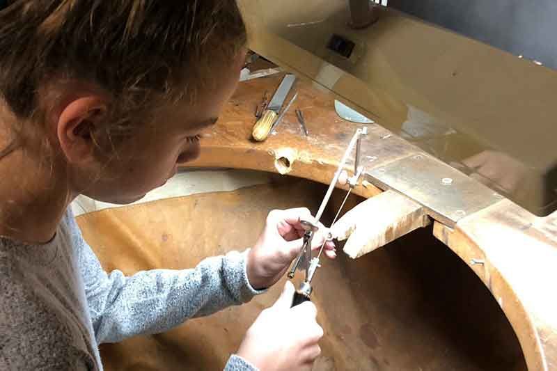 Junge Person sägt konzentriert Metall an der Werkbank eines Juweliers und verwendet dabei Handwerkzeuge.