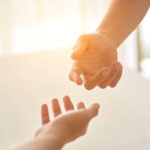 Dos manos que se extienden una hacia la otra en un gesto de ayuda o conexión, bañadas por la cálida y suave luz del sol.