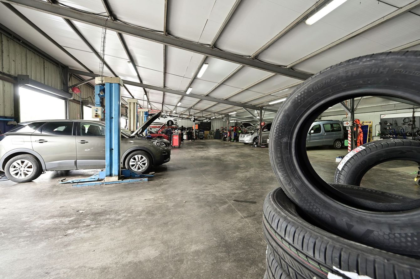 L'atelier mécanique du garage automobile avec plusieurs voitures en arrière-plan et des pneus.