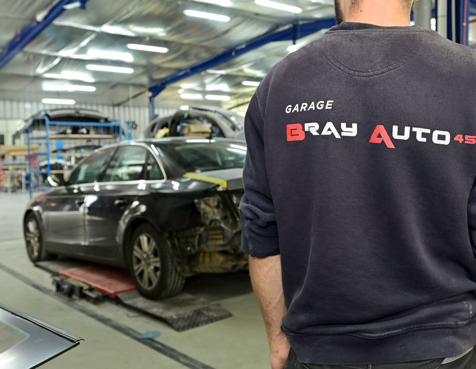 Un technicien du garage dos tourné avec le logo du garage sur son pull.