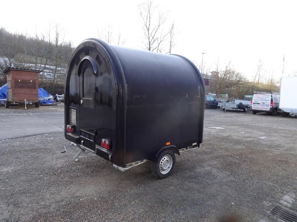 Ein kleiner Anhänger mit einer blauen Plane auf dem Dach steht am Straßenrand.