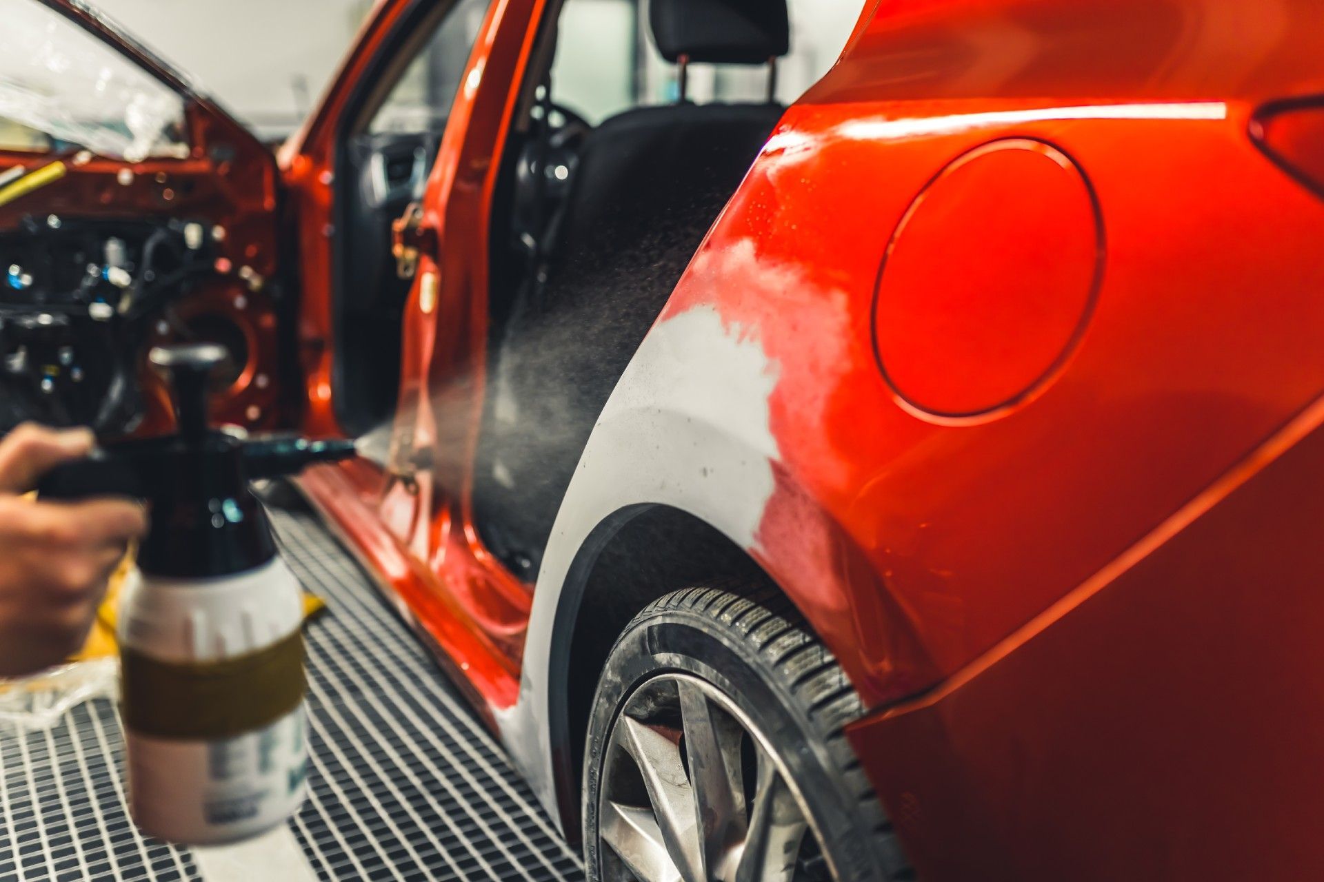 Eine Person sprüht Farbe auf ein rotes Auto in einer Garage.