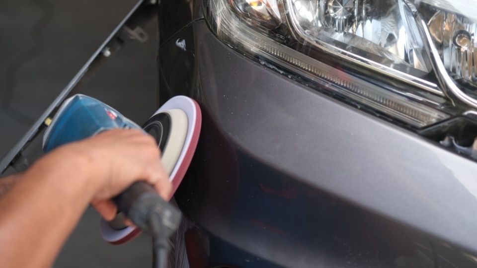 Eine Person poliert die Vorderseite eines Autos mit einem Schleifgerät.