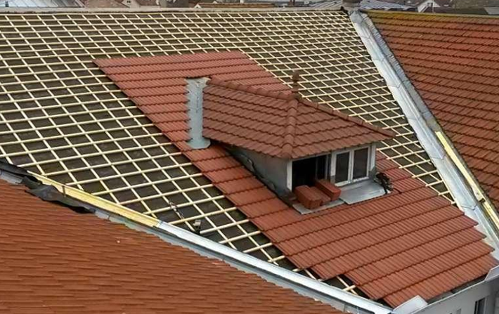 Un toit partiellement couvert de tuiles, avec des lattes de bois apparentes, agrémenté d'une lucarne, donnant sur l'horizon urbain.