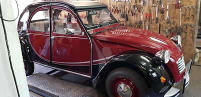 Voiture classique Citroën 2CV bordeaux et noire dans un décor de garage, mettant en valeur son design distinctif.
