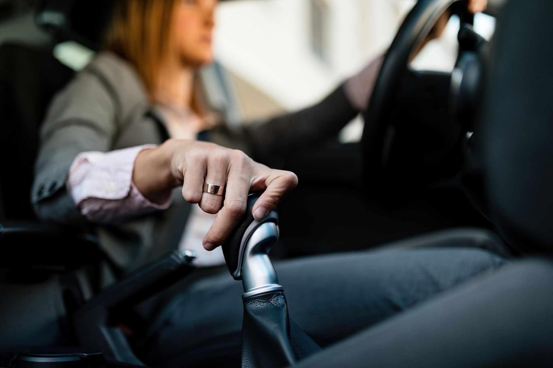 Mano en la palanca de cambios de un coche, con el conductor desenfocado al fondo