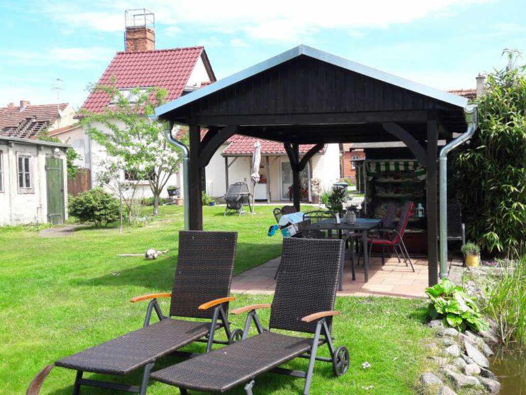 Foto einer Terassenüberdachung aus sehr dunklem Holz mit Strandkorb, Tisch und Stühlen darunter