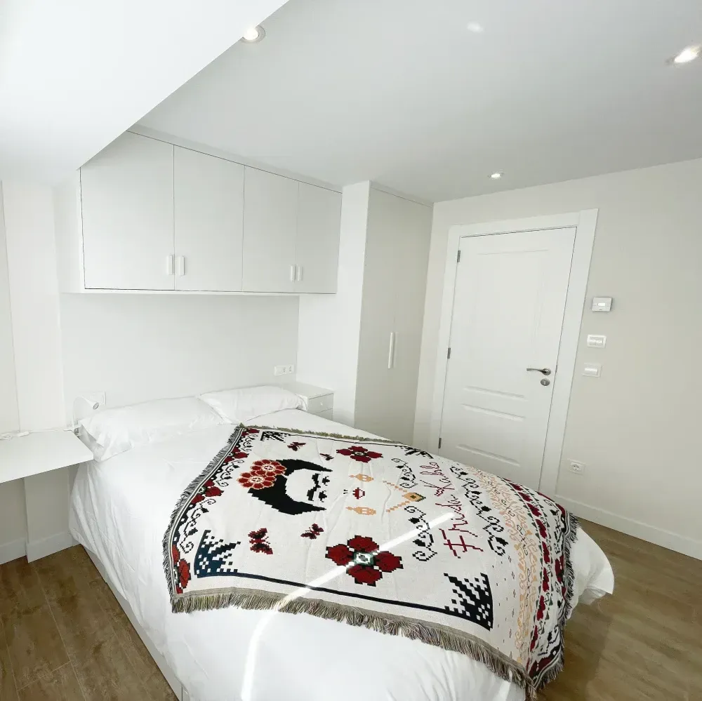 Un dormitorio blanco con una cama con una manta de Frida Kahlo, armarios empotrados, 