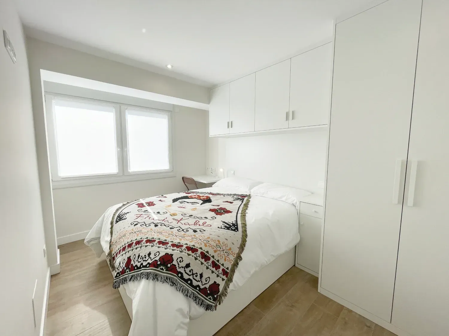 Un dormitorio pequeño, completamente blanco, con una cama con una manta estampada