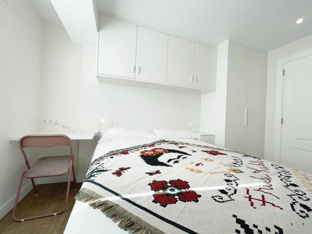 Pequeña habitación blanca con cama, escritorio y armarios.