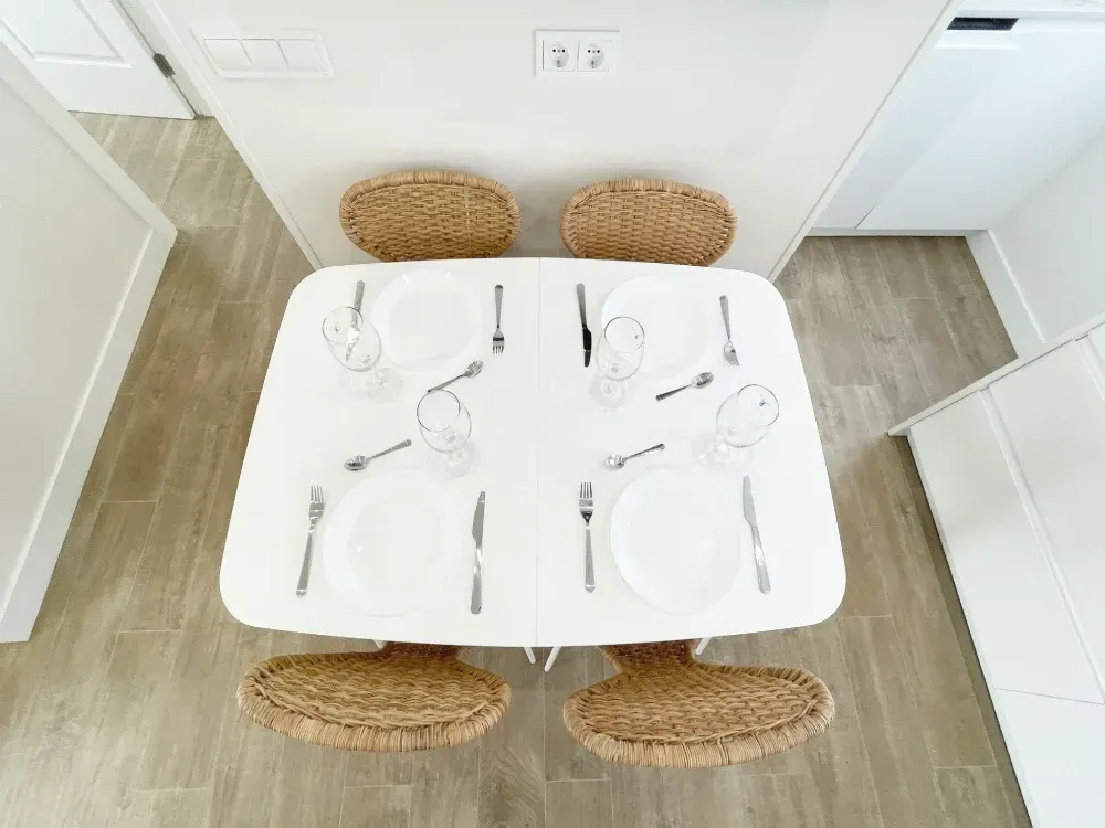 Una pequeña mesa de comedor blanca para cuatro personas con sillas tejidas.