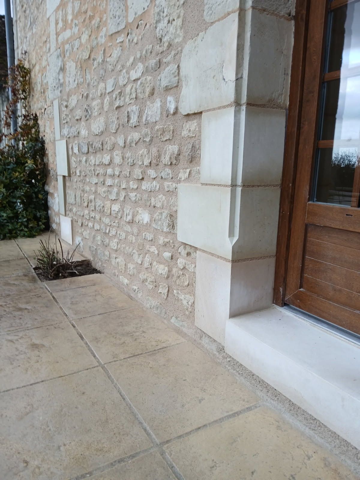 Façade en pierre avec terrasse carrelée et encadrement de porte en bois.