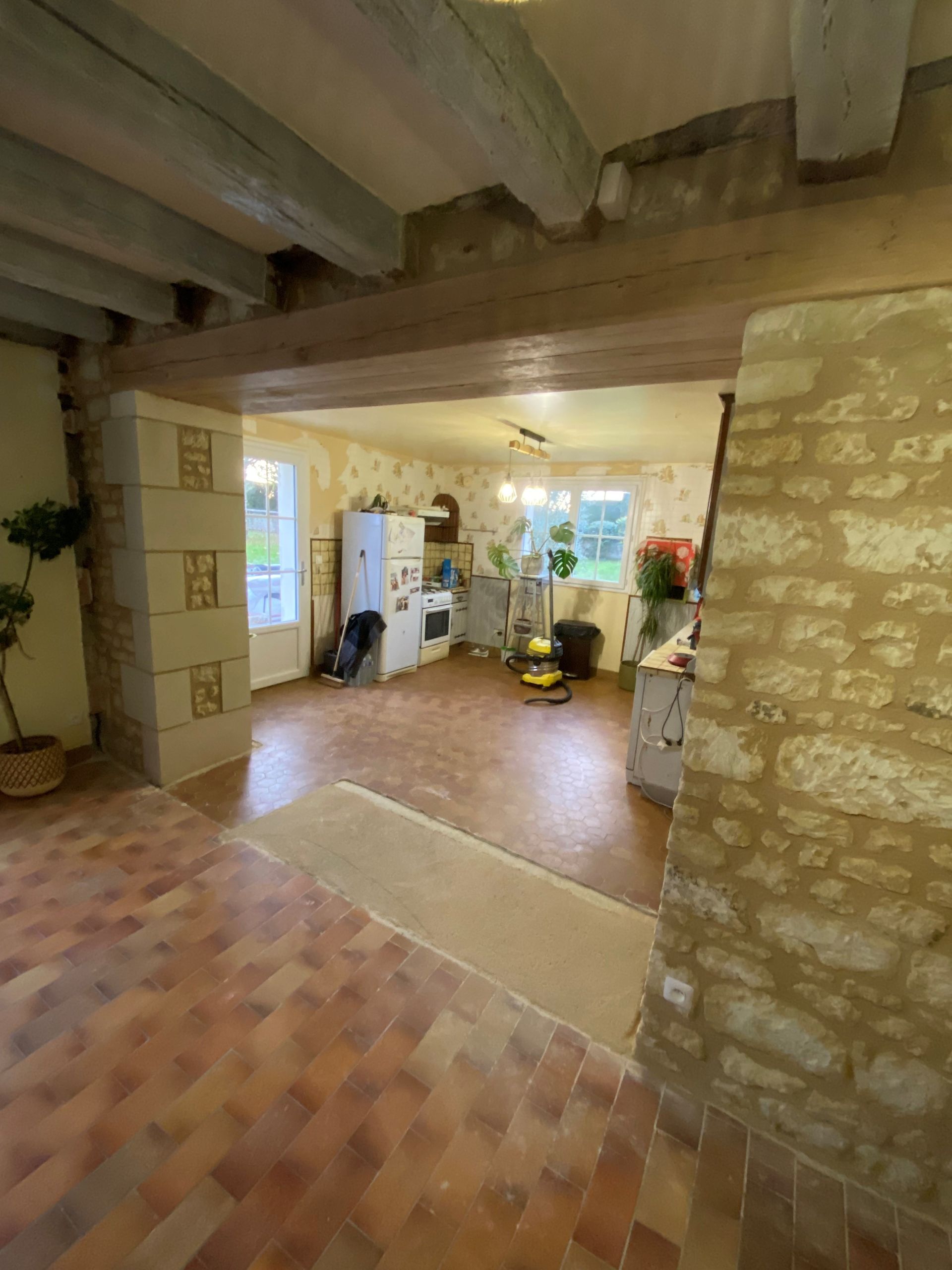 Intérieur de cuisine avec carrelage en terre cuite, poutres apparentes et murs en pierre.