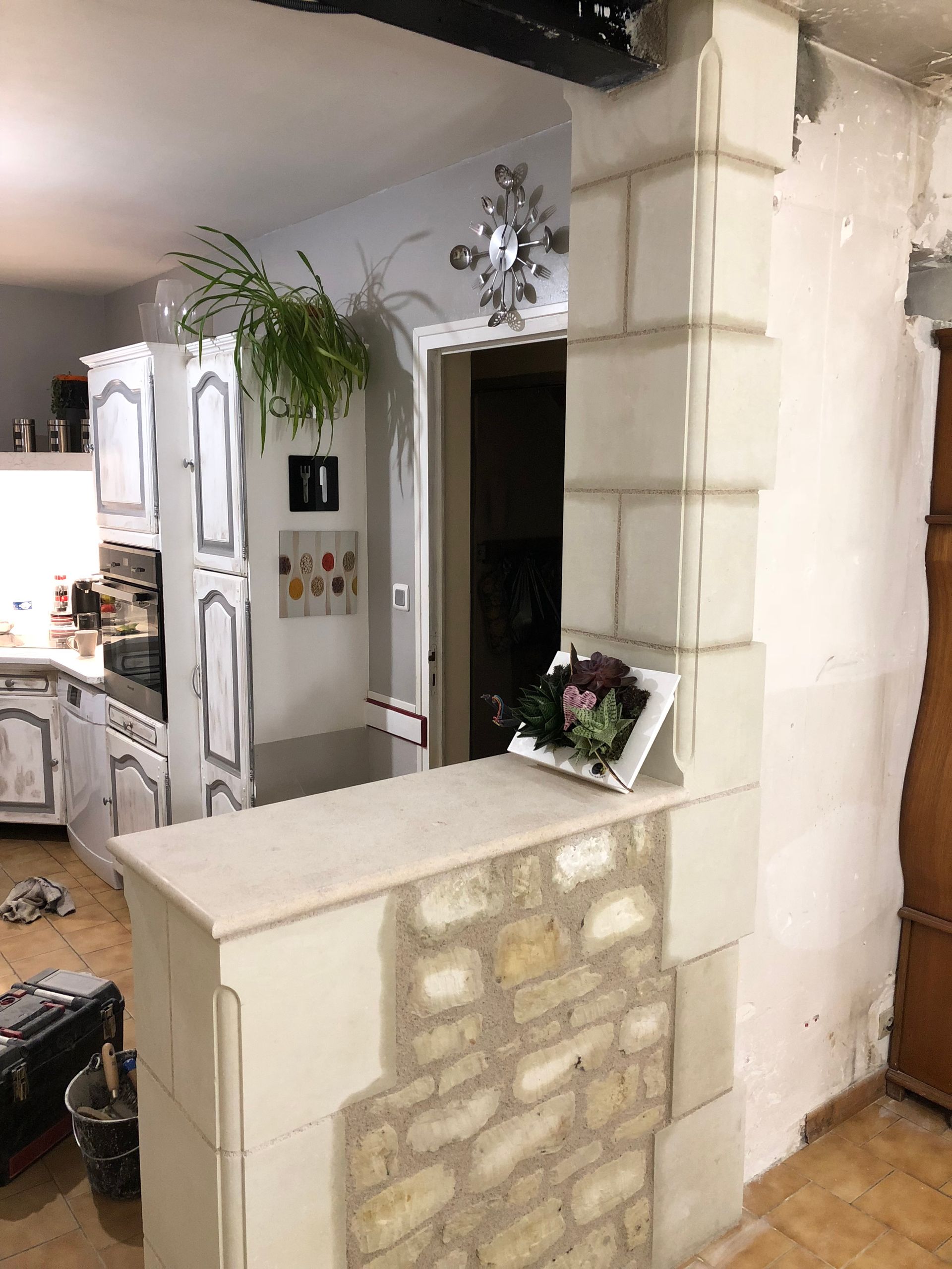 Cuisine avec placards blancs, murs en pierre et une ouverture décorative donnant sur une autre pièce.