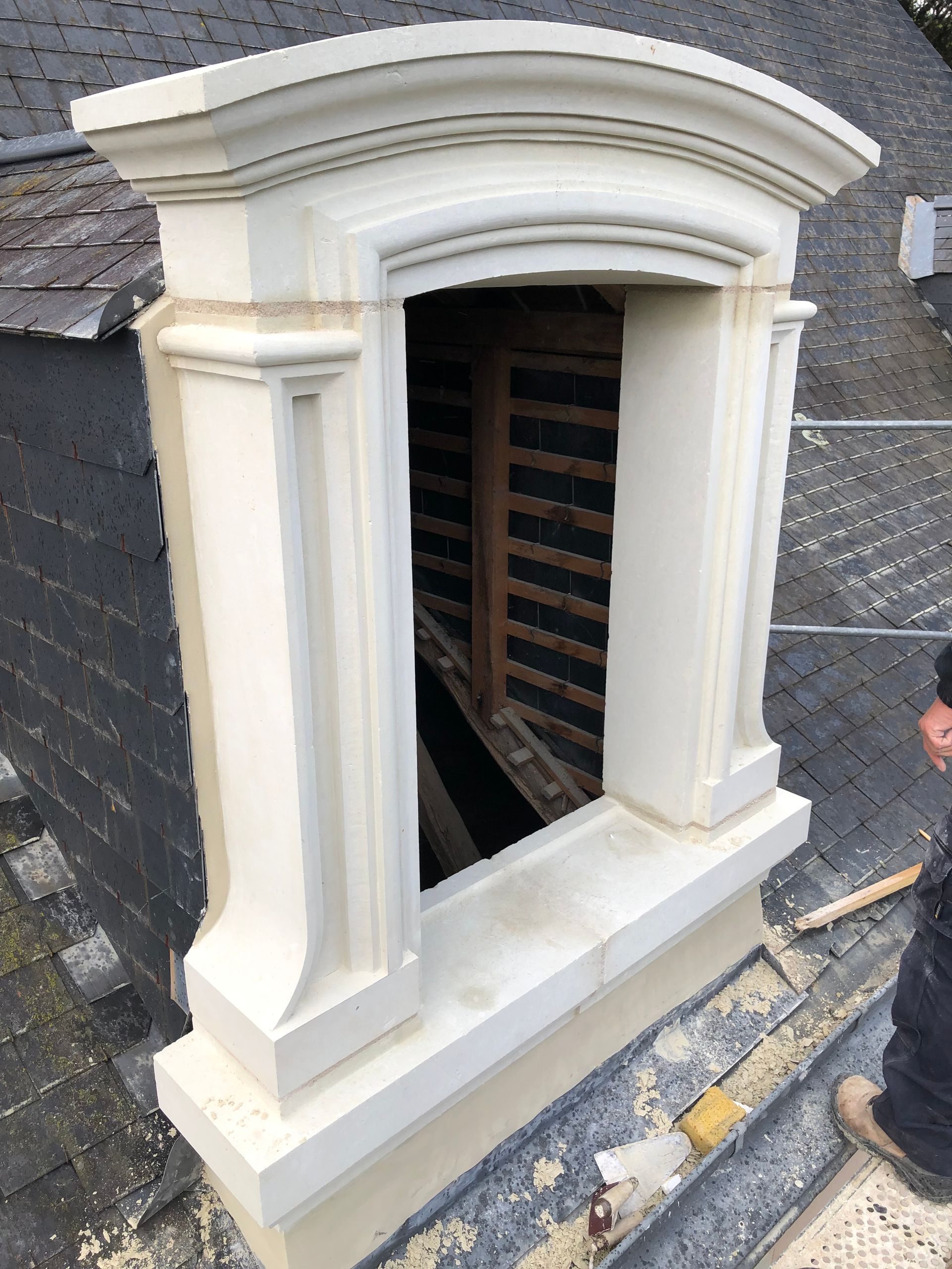 Encadrement de fenêtre en pierre sur un toit d'ardoise.