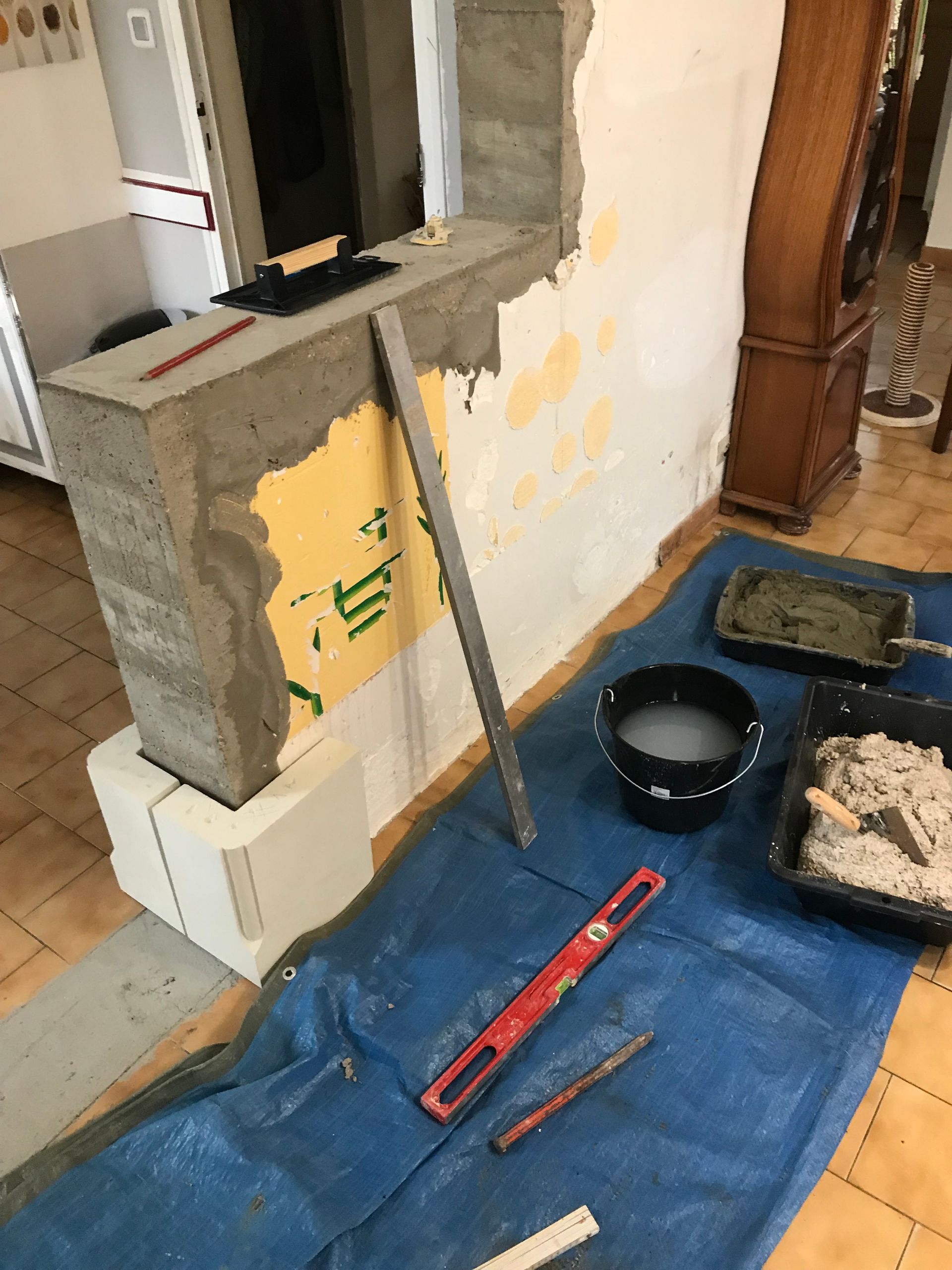 Travaux en cours : un demi-mur avec des travaux de ciment, des outils et des matériaux sur une bâche bleue.