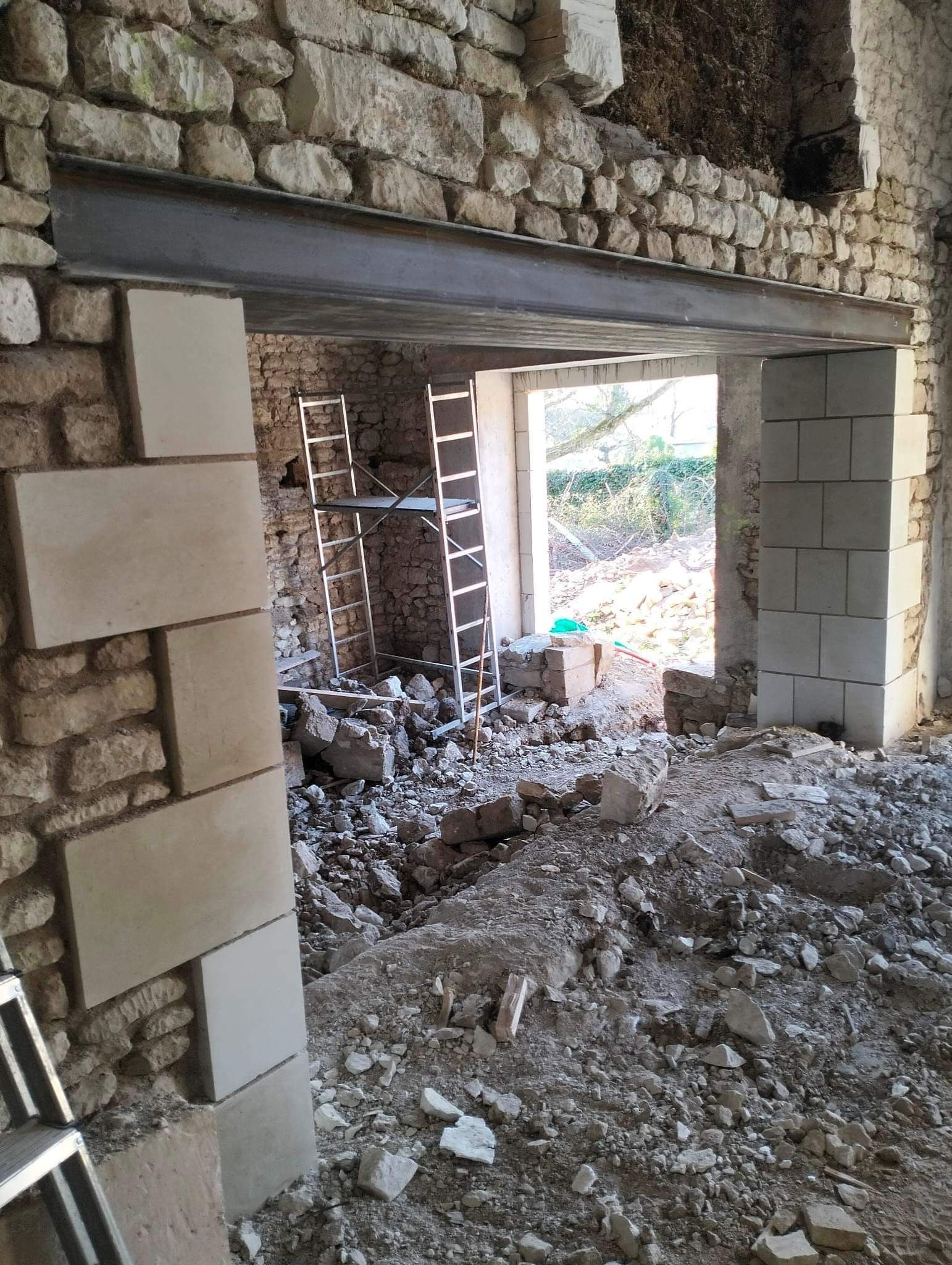 Intérieur d'un bâtiment en construction, montrant un mur de pierre, une poutre d'acier et des gravats.