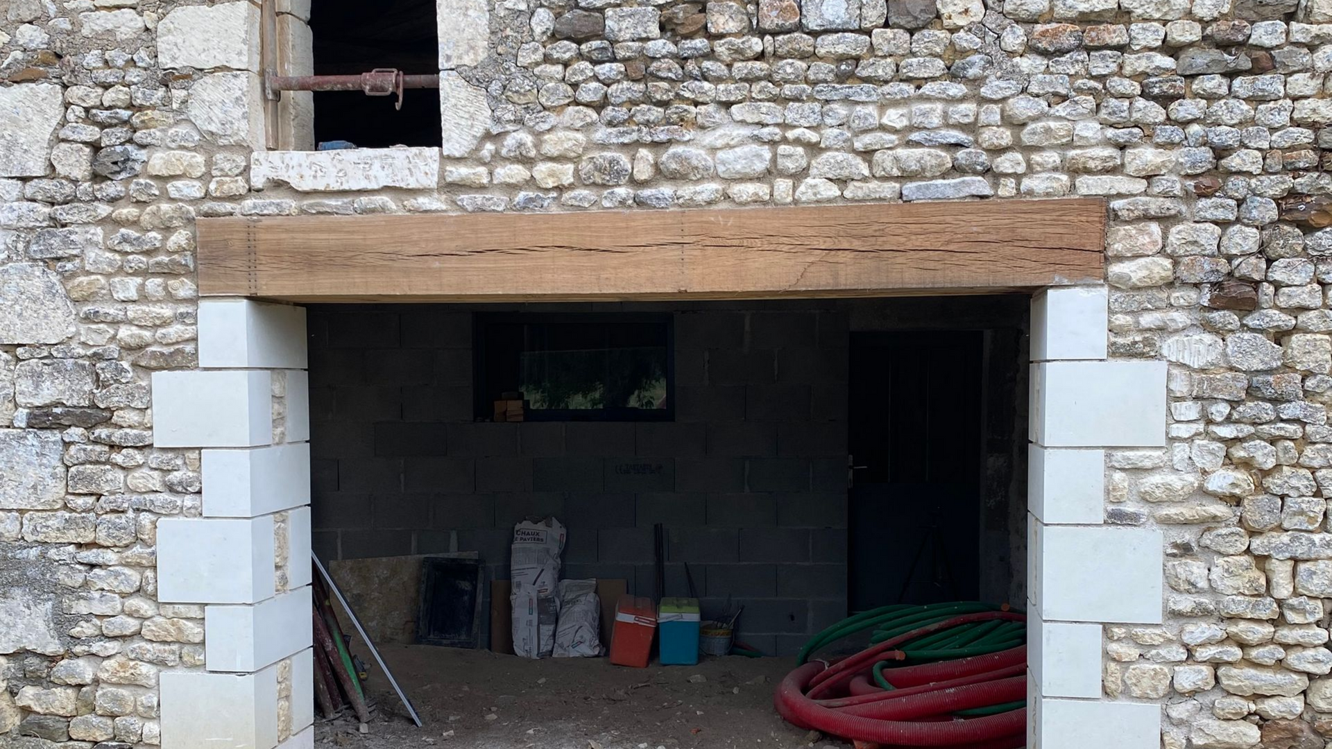 Bâtiment en pierre avec une porte ouverte encadrée de blocs blancs et d'une poutre en bois.