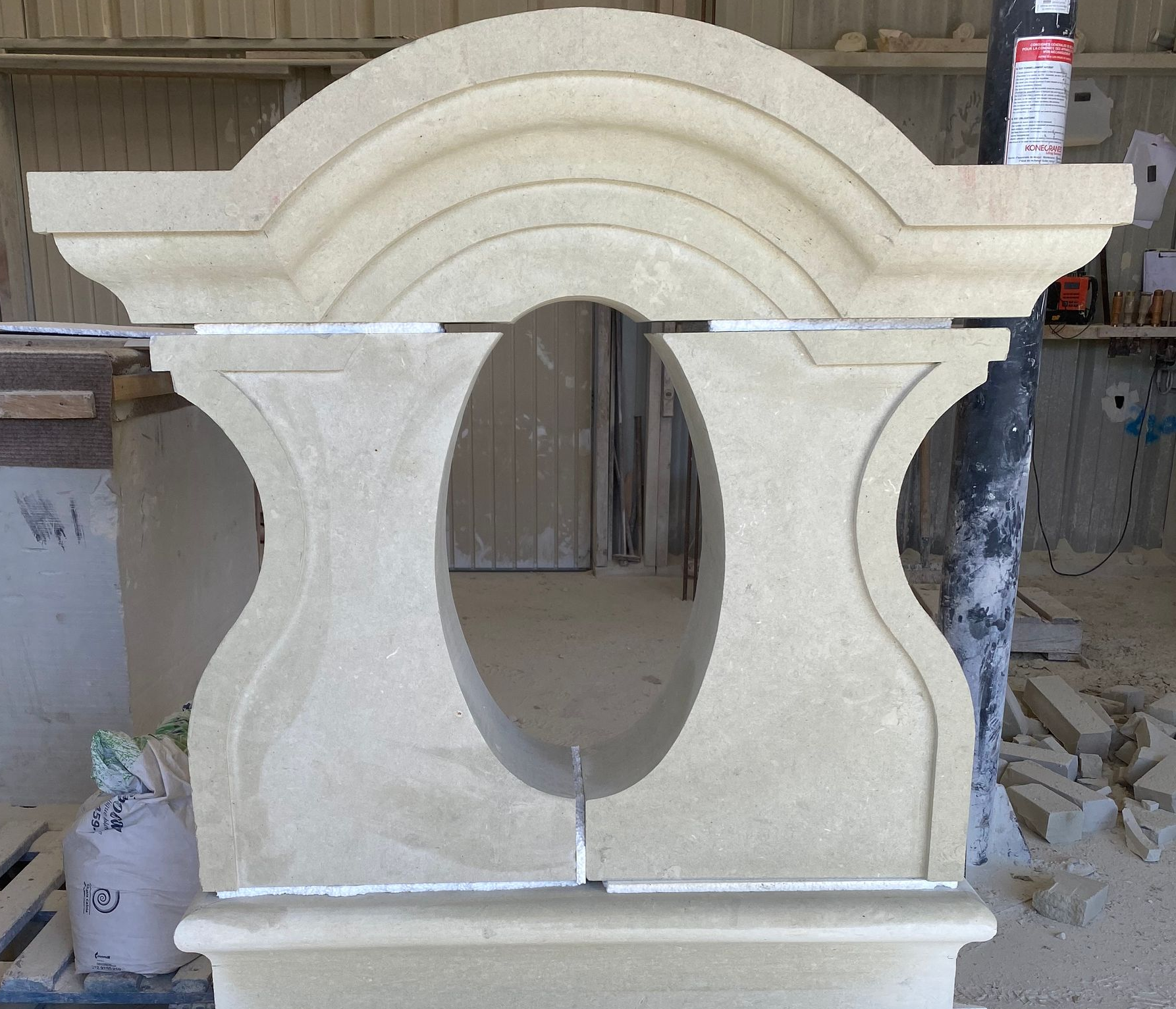 Élément architectural en pierre claire partiellement assemblé, comportant une ouverture ovale, posé sur un plan de travail.