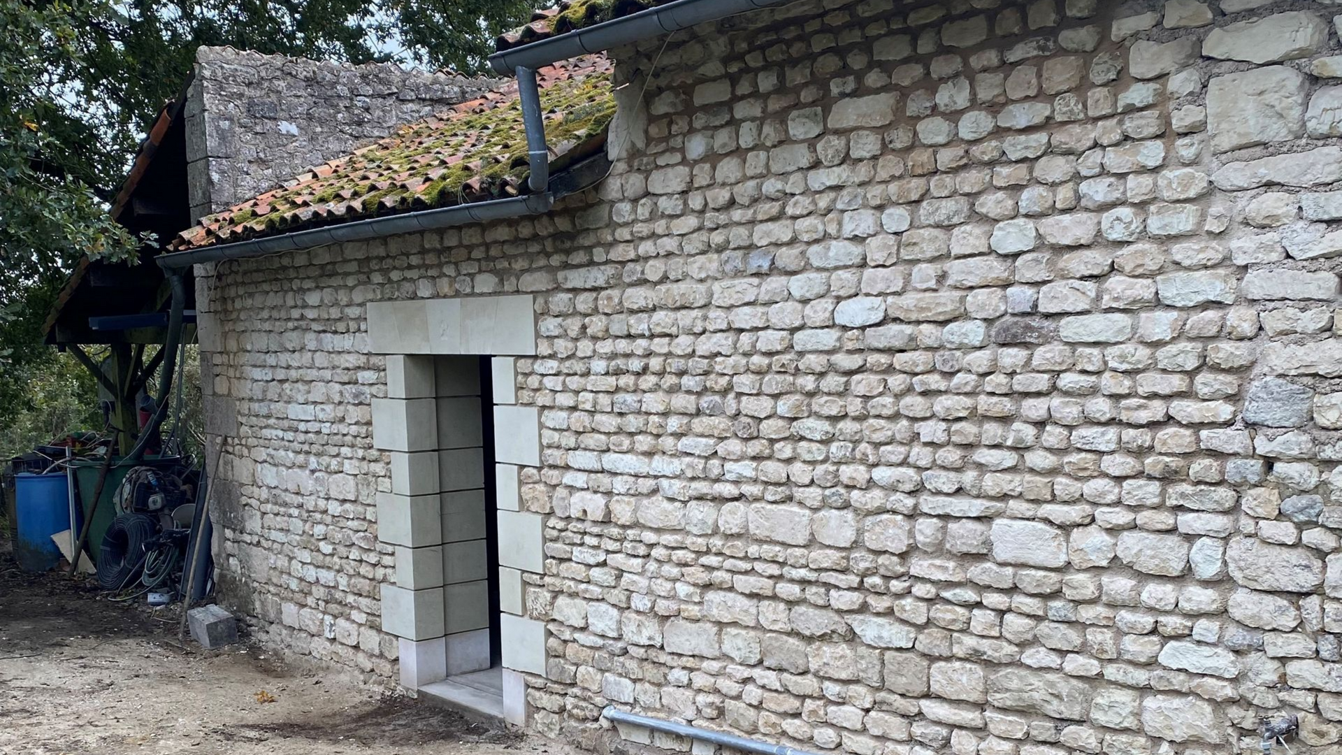 Bâtiment en pierre avec porte ouverte et un toit de tuiles rouges.
