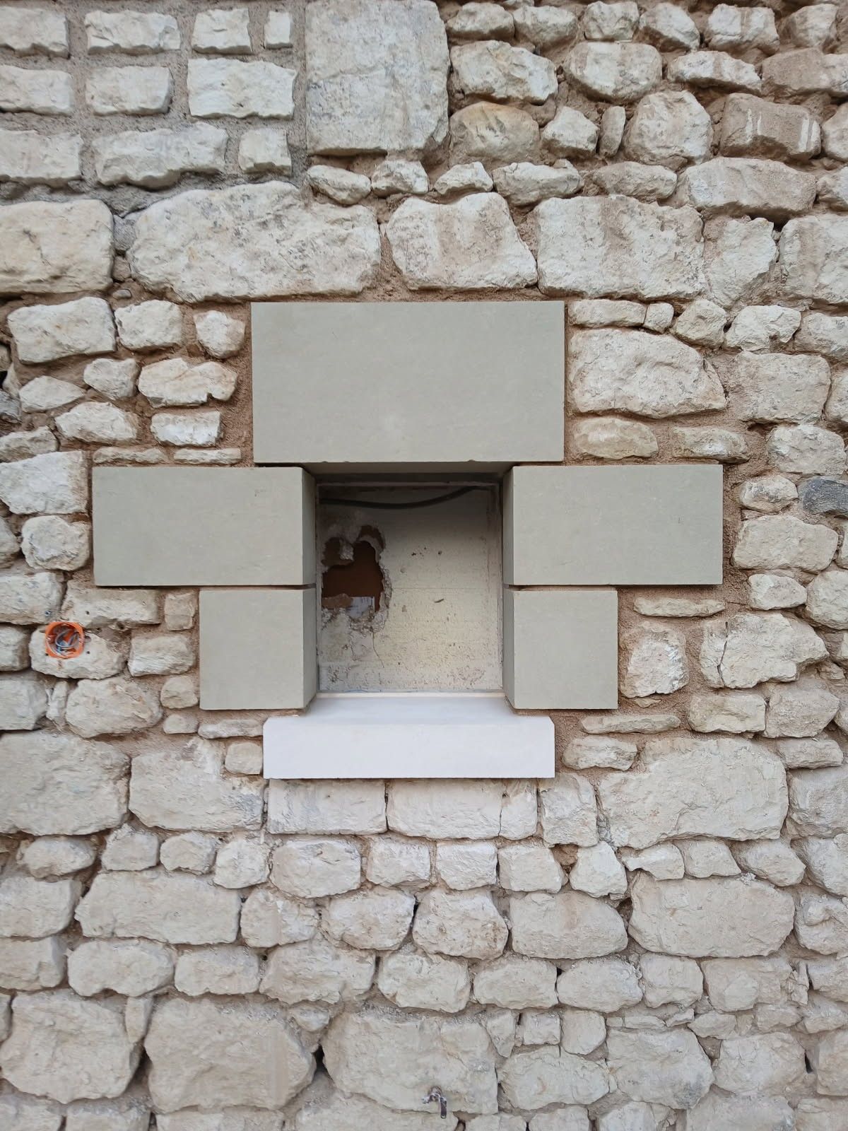 Fenêtre dans un mur de pierre, encadrée de blocs clairs.