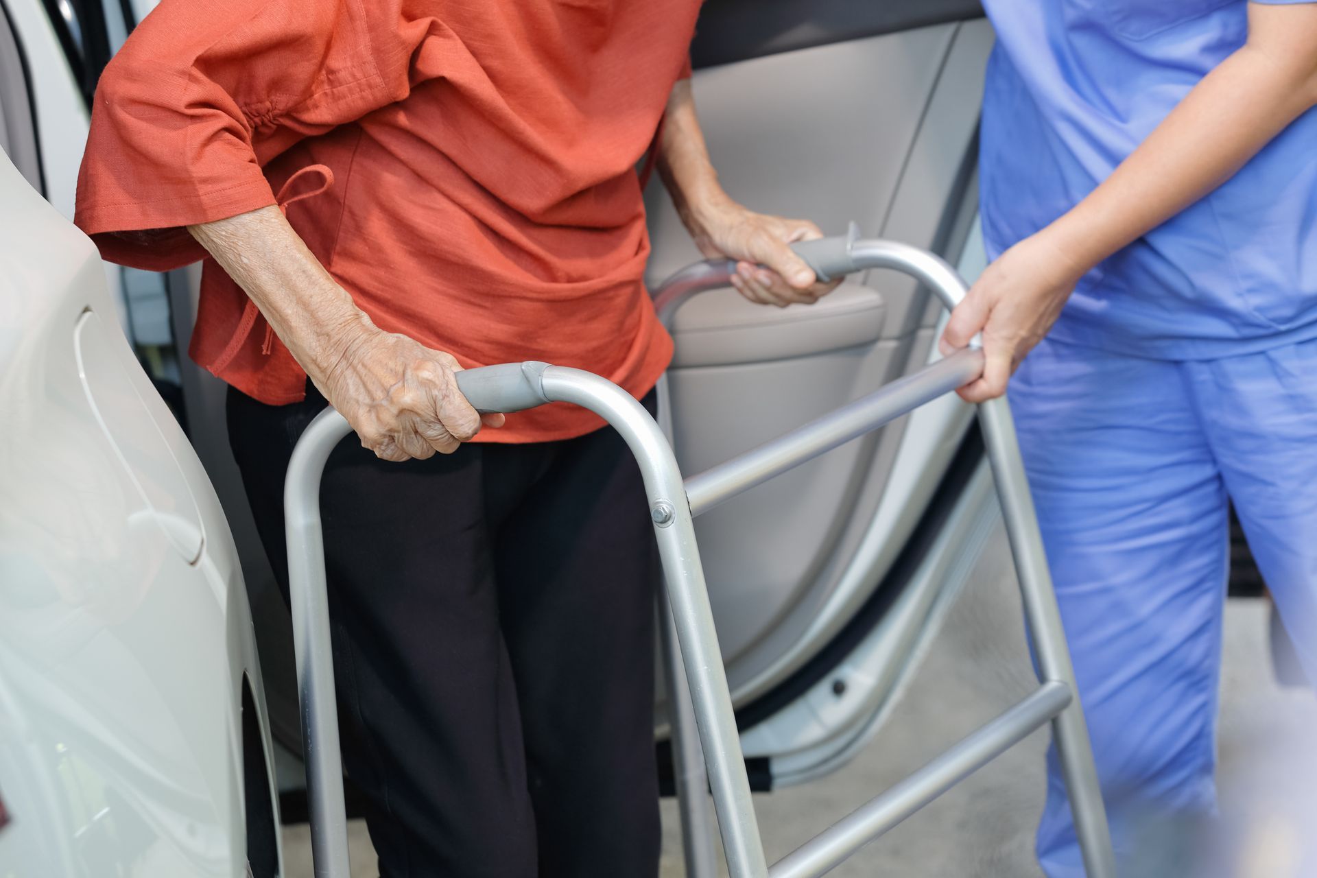 Une personne âgée sortant d'un VSL à l'aide d'un déambulateur