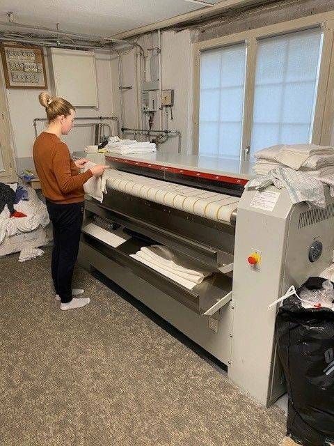 Eine Frau bügelt Wäsche mit einer grossen gewerblichen Bügelmaschine in einem Waschraum.