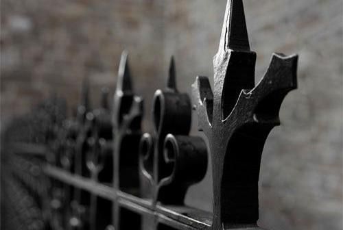 Un primer plano de una valla de hierro forjado con una pared de ladrillos al fondo.