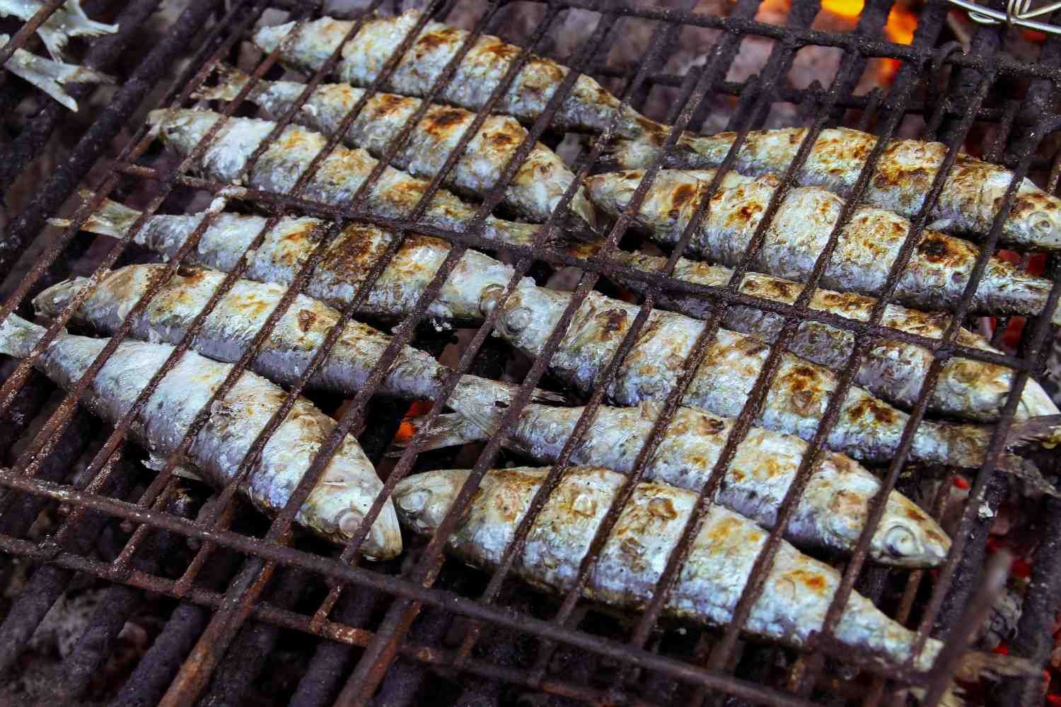 Pescado a la parrilla cocinándose sobre una barbacoa de carbón, con la piel dorada y las rejillas oscuras.