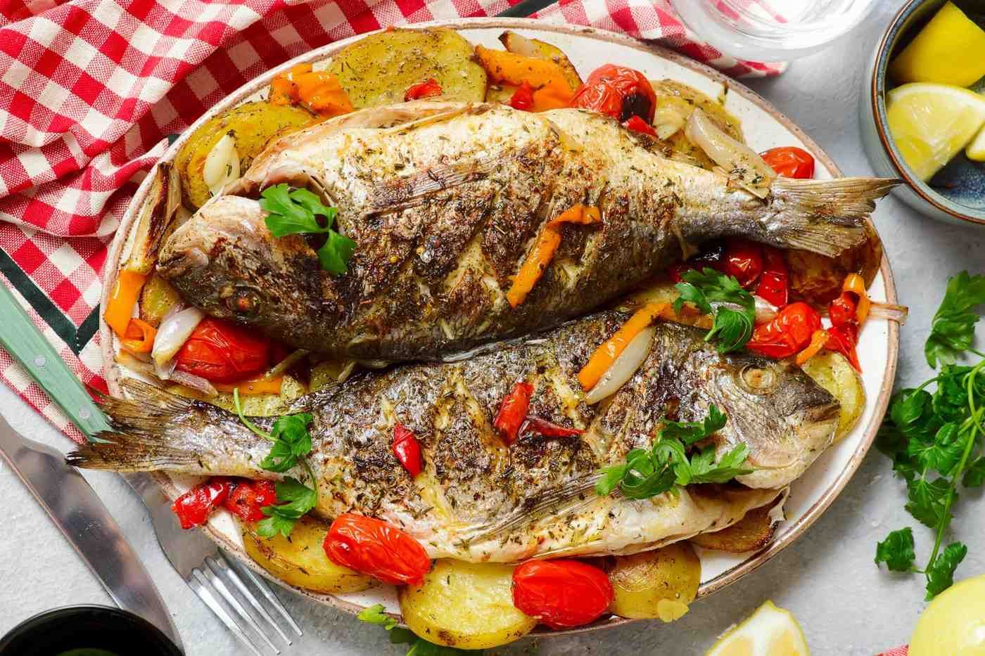Dos pescados al horno en una fuente con verduras asadas y rodajas de limón.