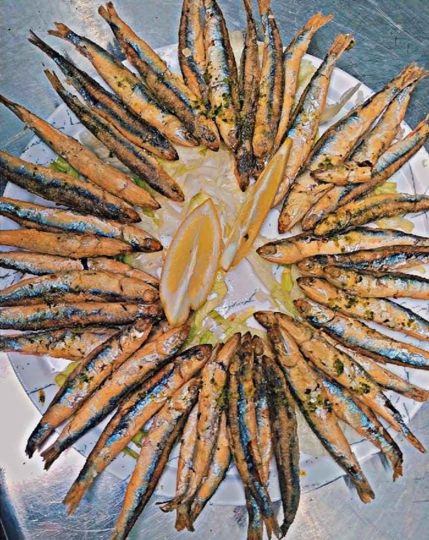 Sardinas a la parrilla dispuestas en círculo sobre un plato con rodajas de limón en el centro.