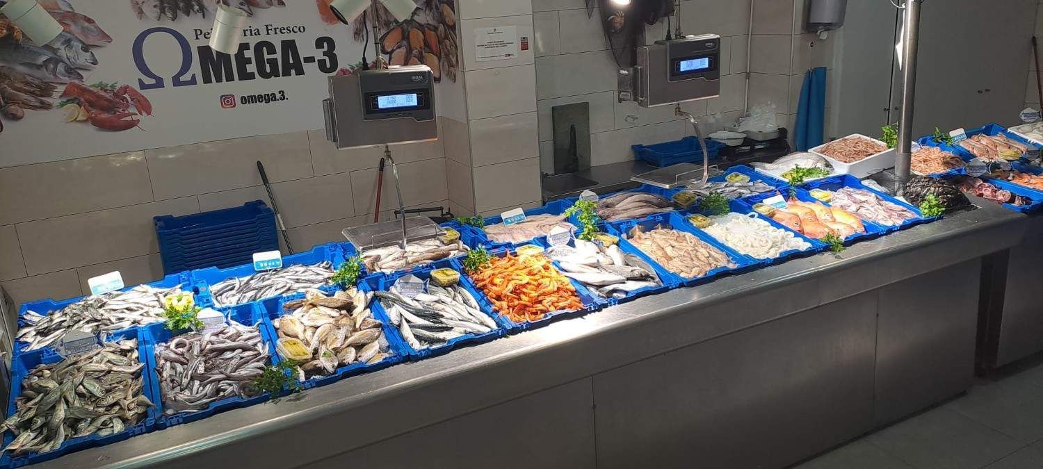 Exhibición de mariscos en el mercado con bandejas de pescado y marisco sobre hielo bajo luces azules.