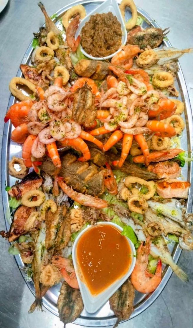 Plato de mariscos variados con camarones, pescado frito, calamares, papas fritas y salsas para mojar en una bandeja grande.