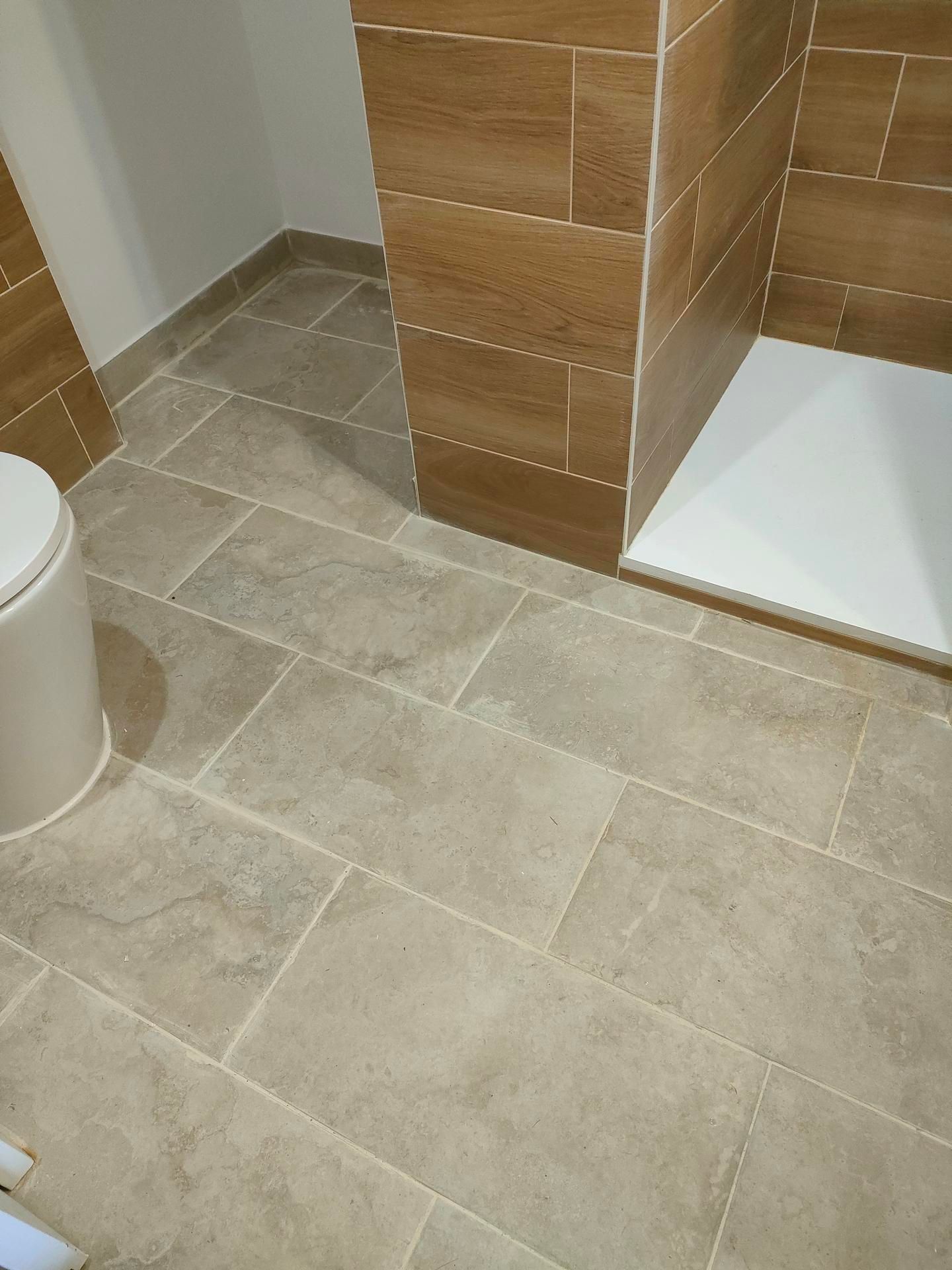 Salle de bains avec carrelage beige au sol, carrelage mural imitation bois dans la douche et receveur de douche blanc.