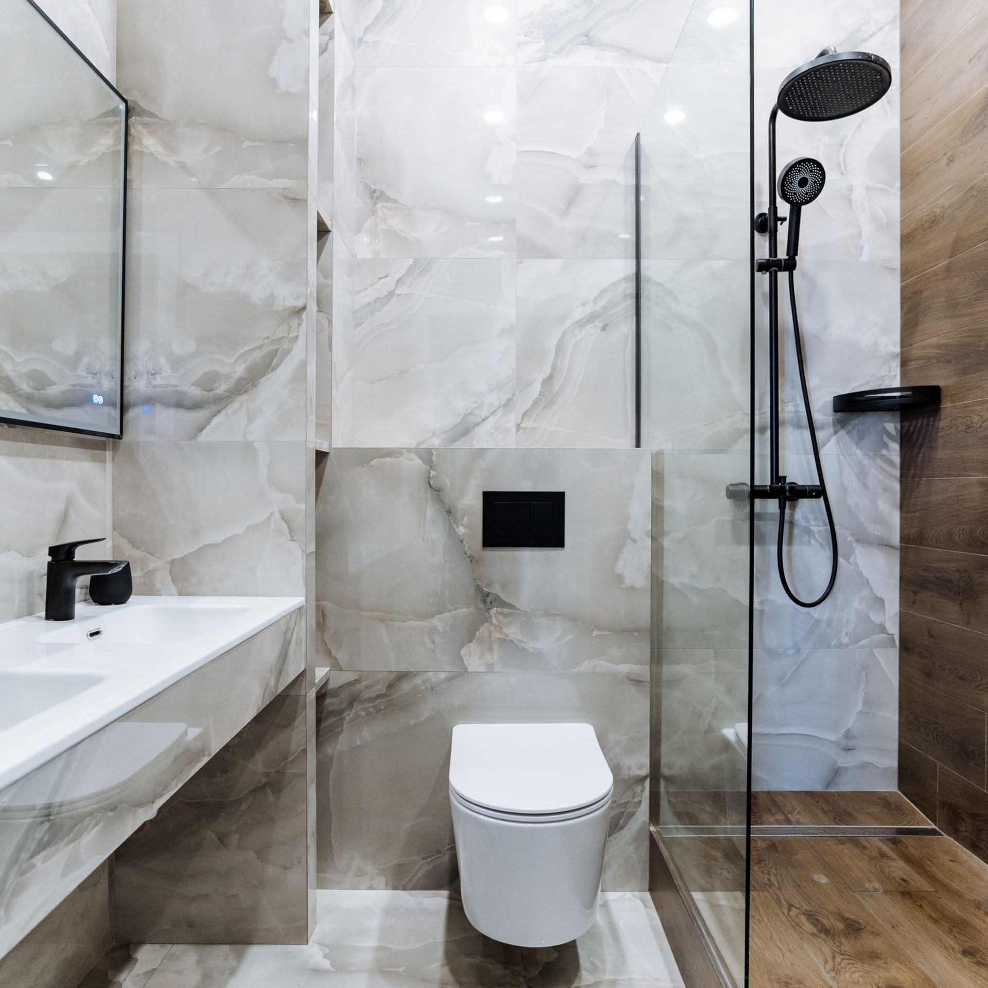 Salle de bains moderne avec carrelage en marbre blanc et gris, robinetterie noire et porte de douche en verre.