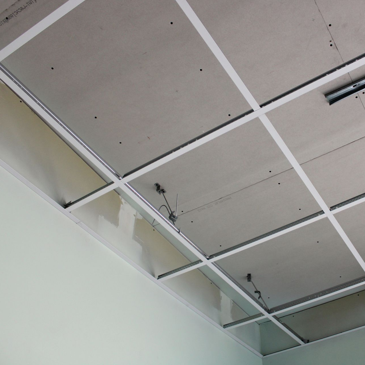 Construction d'un plafond suspendu avec une grille métallique blanche et des panneaux gris.