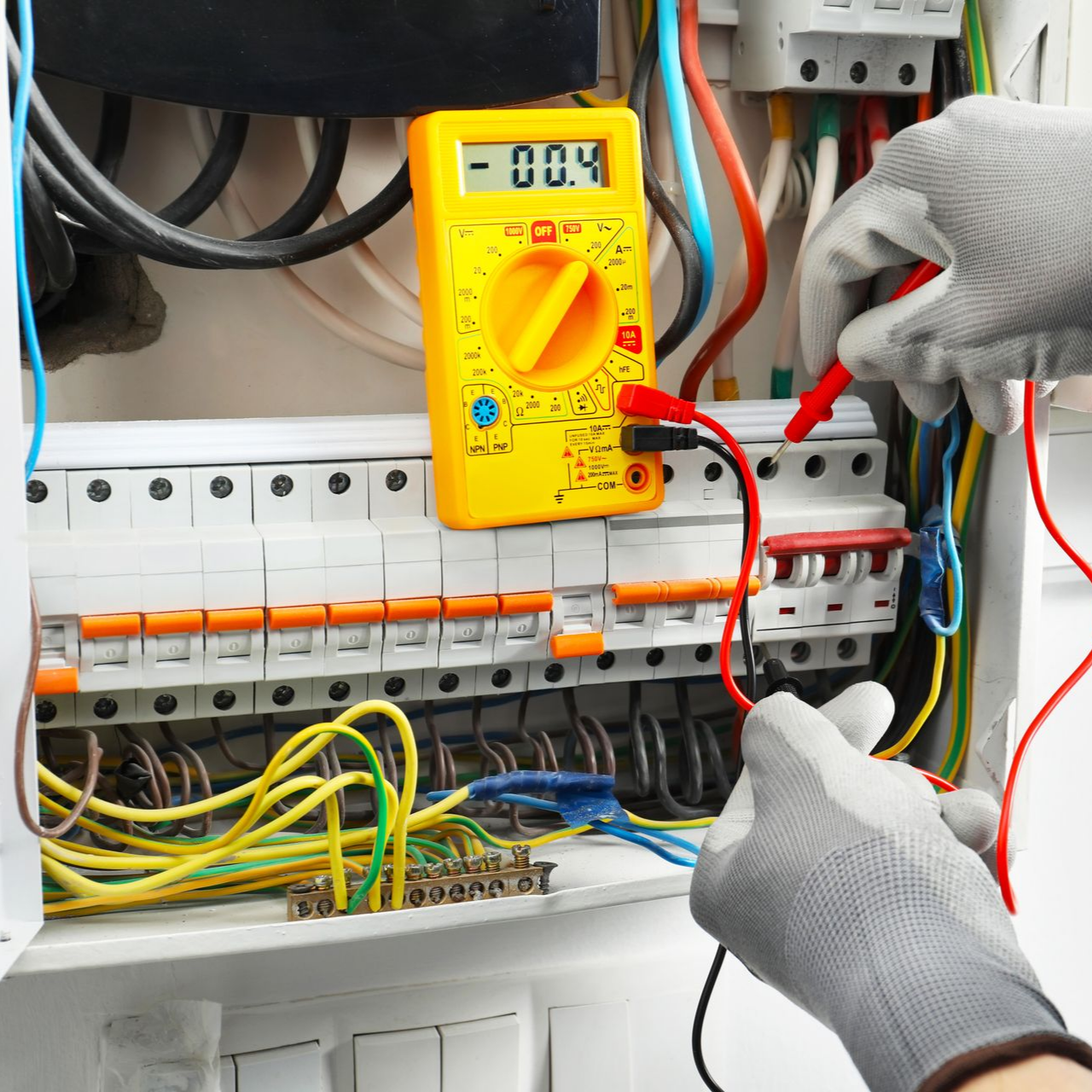 Électricien testant un tableau électrique avec un multimètre ; mains gantées, fils électriques.