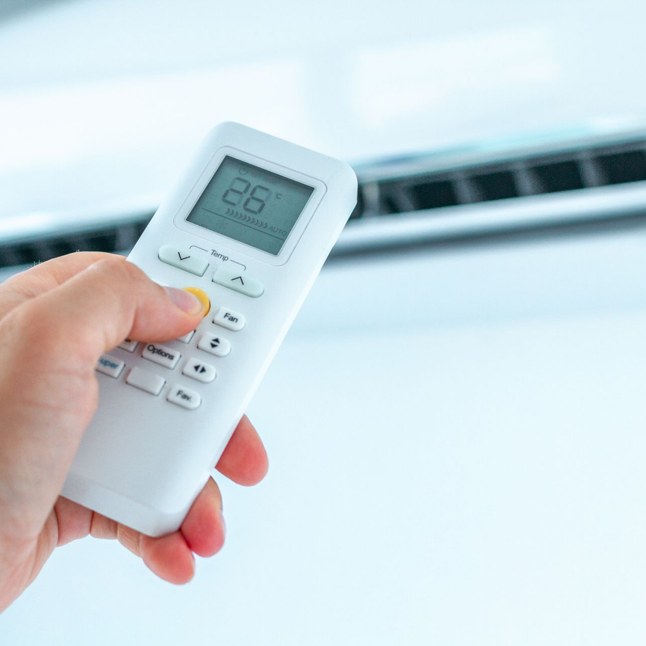 Main tenant la télécommande du climatiseur, réglant la température à 26°C.