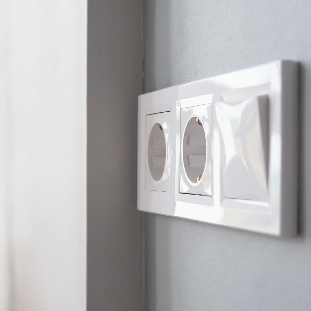 Prise électrique et interrupteur blancs sur un mur gris.