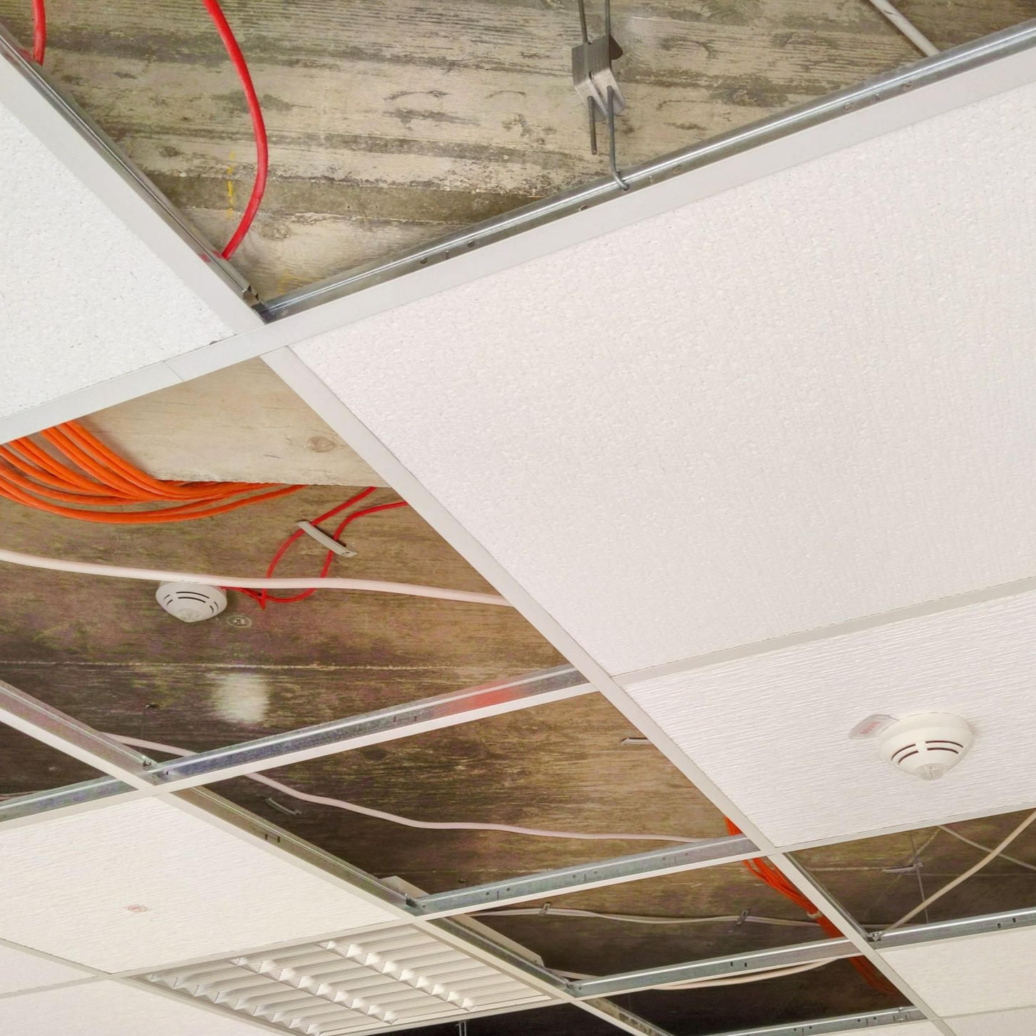 Plafond suspendu en construction, câbles et ossature apparents.