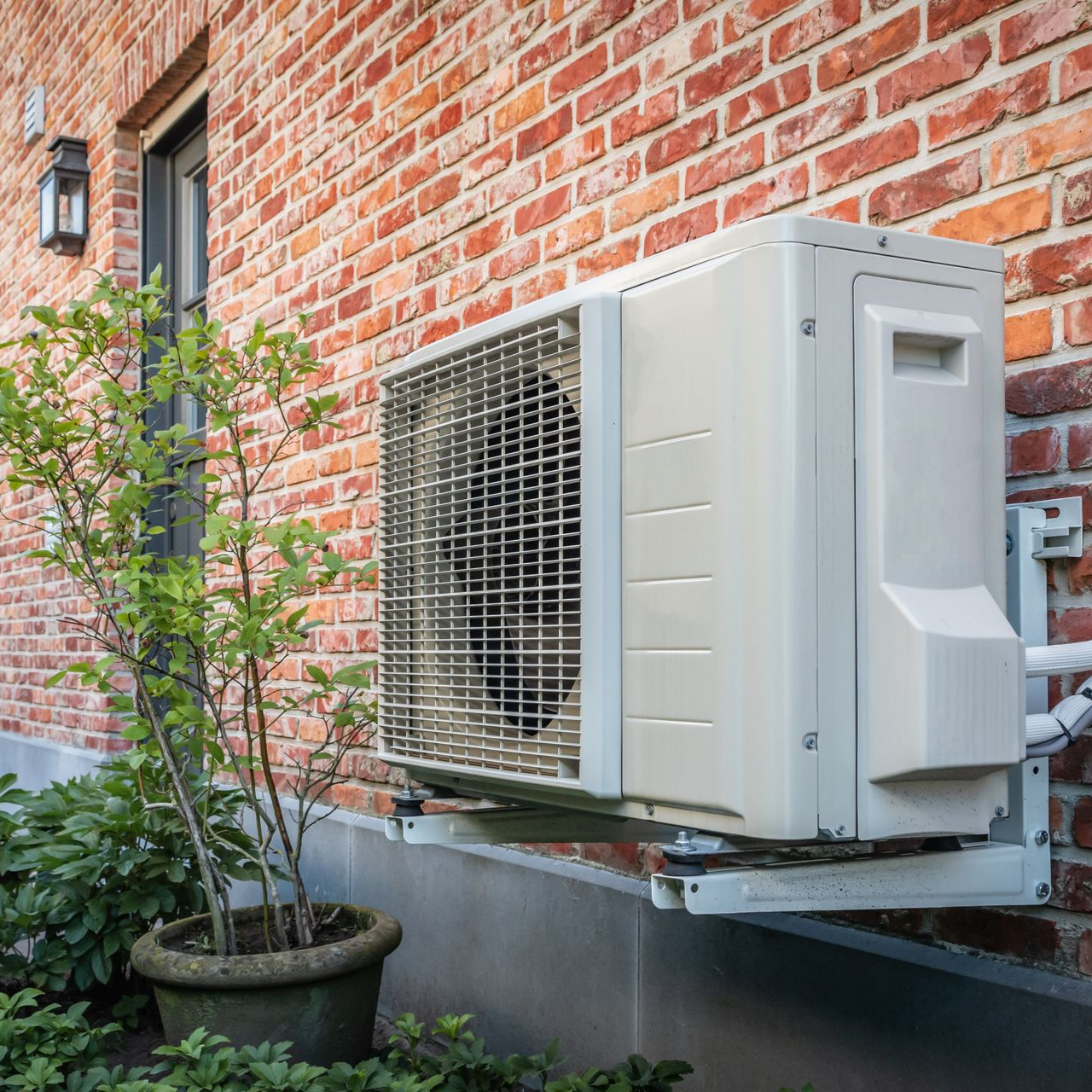 Unité de climatisation fixée sur un mur de briques à côté d'une plante en pot.