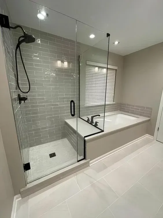 Salle de bains moderne avec douche en verre, baignoire, carrelage gris clair et sol blanc.
