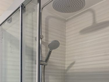 Douche avec porte en verre, pommeaux de douche de tête et à main sur une barre métallique, mur carrelé.