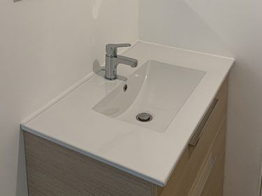 Meuble-lavabo de salle de bains avec lavabo blanc, robinet chromé et armoire en bois.