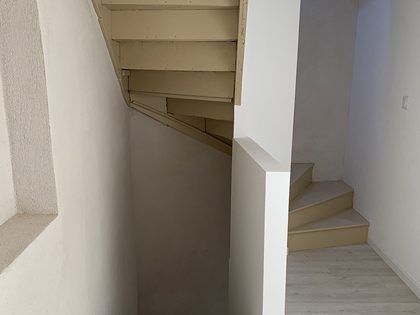 Escalier aux marches en bois et aux murs blancs ; vu d’en bas. L’escalier monte et descend.