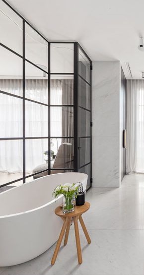 Une salle de bains moderne avec une baignoire îlot, une douche à parois de verre et un petit tabouret en bois.